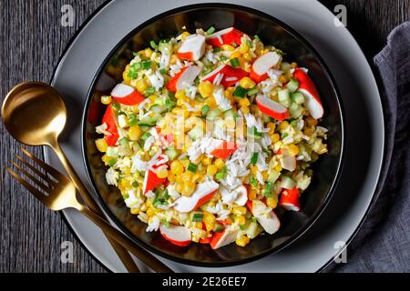 Salade de crabe de bâtonnets de surimi aux légumes : maïs, concombres, scallion, œufs, riz jasmin avec sauce lime et mayonnaise servi dans un bol noir o Banque D'Images