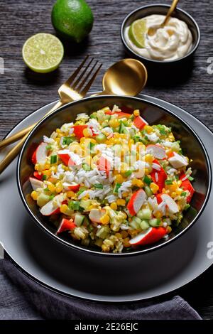 Salade de crabe de bâtonnets de surimi aux légumes : maïs, concombres, scallion, œufs, riz jasmin avec sauce lime et mayonnaise servi dans un bol noir o Banque D'Images