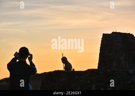 Ruines de Pompéi. Jeune touriste avec carte en main prenant des photos avec un smartphone des ruines de Pompéi avec un mur détruit et une statue de guerrier au coucher du soleil. Banque D'Images