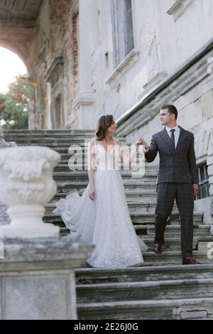 Mariée et marié descendant par des escaliers dans le vieux palais et regardant l'un l'autre. Couple de mariage. Photo de mariage Banque D'Images