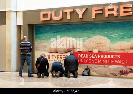 Les passagers musulmans prient en attendant des vols dans le hall des départs près des boutiques hors taxes de l'aéroport international Ben Gurion. Tel-Aviv, Israël. Banque D'Images