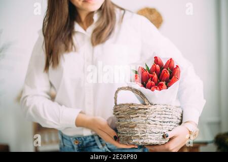 fleuriste femme tenant un panier avec des tulipes rouges dans le papier blanc. concept de livraison de magasin de fleurs Banque D'Images