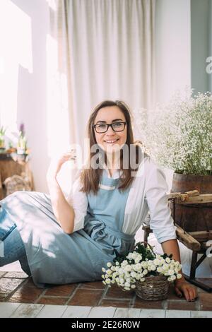 Belle jeune fille brunette dans un tablier parmi la boutique de fleurs. Concept de printemps, bouquets de fleurs fraîches. Banque D'Images