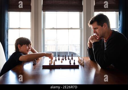 Père et fils assis à une table à l'intérieur jouant une partie d'échecs. Banque D'Images