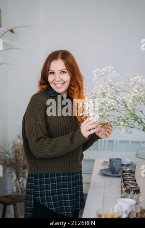 Belle jeune fille de gingembre dans un tablier parmi la boutique de fleurs. Concept de printemps, bouquets de fleurs fraîches. Banque D'Images