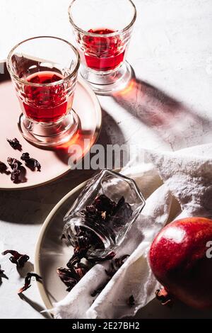 Thé aux fruits frais en verres, grenade mûre sur l'assiette, thé à l'hibiscus et pétales de rose secs, lumière dure avec ombres dures Banque D'Images