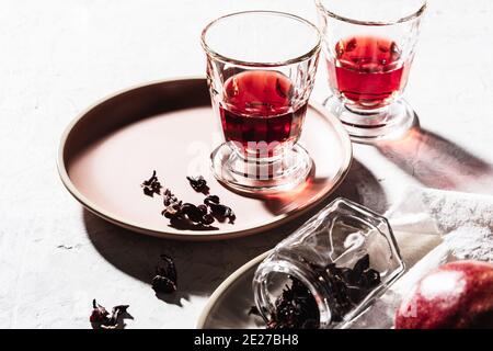 Thé aux fruits frais en verres, grenade mûre sur l'assiette, thé à l'hibiscus et pétales de rose secs, lumière dure avec ombres dures Banque D'Images