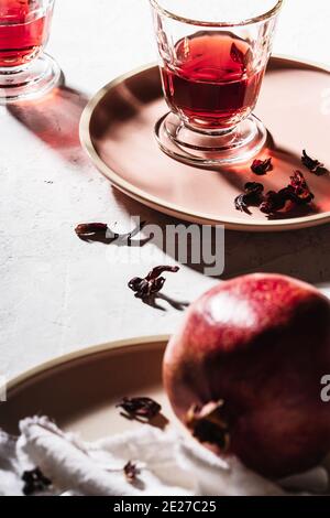 Thé aux fruits frais en verres, grenade mûre sur l'assiette, thé à l'hibiscus et pétales de rose secs, lumière dure avec ombres dures Banque D'Images