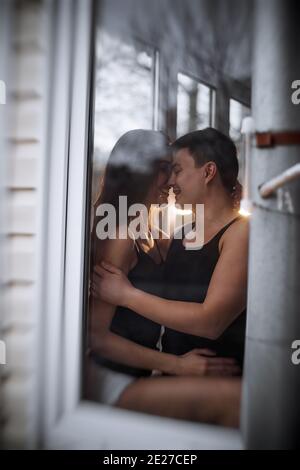 Un jeune couple aimant se hale dans la fenêtre de leur balcon terrasse dans l'appartement. Un jeune homme rit avec une belle femme à la maison. Amoureux baiser, passer Banque D'Images