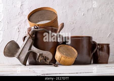 Un pot en argile, une passoire en bois et un dispositif en métal pour le jus contre un mur blanc. Anciens accessoires dans la maison. Arrière-plan clair. Banque D'Images
