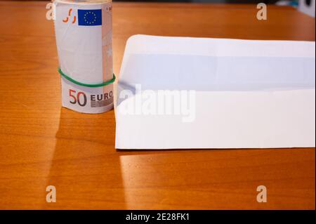Un chèque de paie blanc a été ouvert sur une table en bois: À côté d'elle un rouleau volumineux de 50 euros de factures fixées par un élastique vert. Image conceptuelle de salaire. Banque D'Images