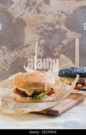 Deux hamburgers de bœuf faits maison avec des légumes verts, des oignons rouges, des tomates, des concombres marinés et du fromage Banque D'Images