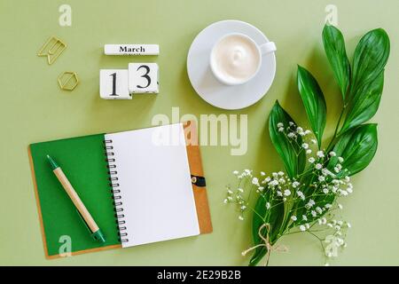 Calendrier des cubes en bois Mars 13. Bloc-notes, tasse de café, bouquet de fleurs sur fond vert. Concept Hello Spring Creative vue du dessus maquette de pose plate. Banque D'Images