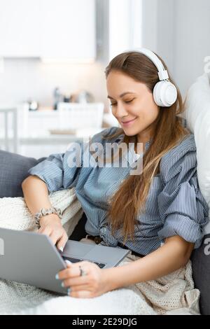 Femme caucasienne pendant une conversation en ligne. Elle a un appel vidéo pendant qu'elle est assise sur le canapé à la maison. Concept de technologie moderne. Photo verticale. Banque D'Images