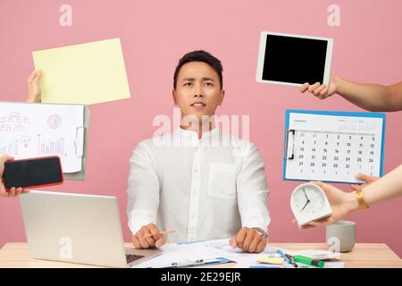 Jeune homme triste se trouve au bureau, mains avec des papiers, réveil, touchpad, le bloc-notes avec des autocollants, des études, de la documentation plus isolé sur fond rose Banque D'Images