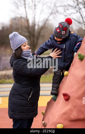 POZNAN, POLOGNE - 10 janvier 2021 : mère aidant un jeune garçon sur un mur d'escalade dans un terrain de jeu du parc Rataje. Banque D'Images