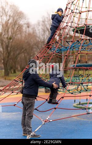 POZNAN, POLOGNE - 10 janvier 2021 : homme et enfants à côté d'un équipement de montée dans une aire de jeux du parc Rataje. Banque D'Images