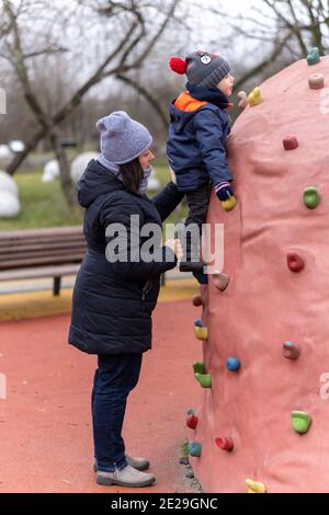 POZNAN, POLOGNE - 10 janvier 2021 : mère aidant un jeune garçon sur un mur d'escalade dans un terrain de jeu du parc Rataje. Banque D'Images