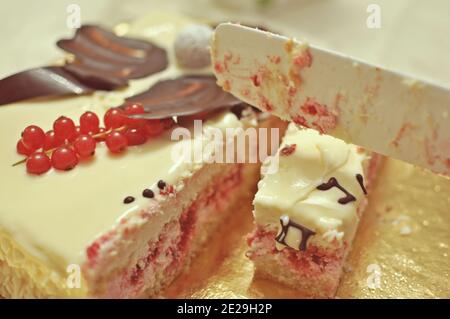 Gros plan d'un couteau coupant un morceau de sucré gâteau blanc à la crème aux fruits (tarte) Banque D'Images