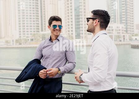 Deux jeunes hommes d'affaires modernes à Dubai Marine se sont penchés sur la clôture. Se tenir debout et discuter des affaires. Banque D'Images