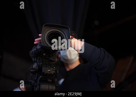 un caméraman masqué filme un spectacle télévisuel en studio. TÉLÉVISION Banque D'Images