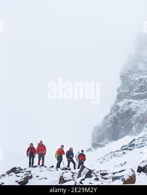 Les touristes masculins avec des sacs à dos et des bâtons de randonnée font une pause pendant la randonnée dans les montagnes d'hiver. Groupe d'alpinistes debout sur des rochers couverts de neige. Concept de voyage, de tourisme et d'alpinisme. Banque D'Images