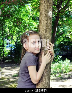 Enfant blond, fille, 8 ans, souriant et embrassant un arbre de tronc dans la forêt Banque D'Images