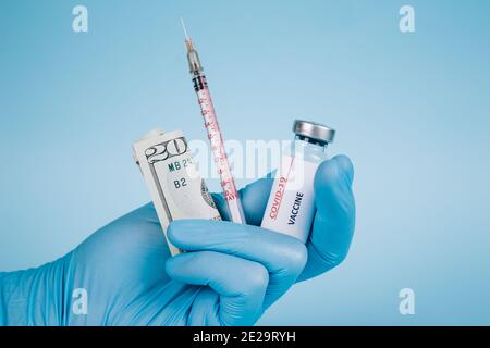 Lviv, Ukraine - 29 décembre 2020 : médecin détenant une facture de 20 dollars et une dose en flacon du vaccin COVID-19 avec seringue sur fond bleu avec copie Banque D'Images