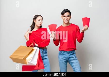 Couple asiatique heureux avec sacs de shopping et enveloppes rouges isolées En studio gris pour le concept chinois de vente du nouvel an Banque D'Images