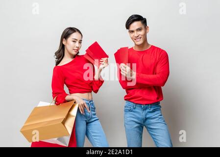 Un couple asiatique heureux avec des sacs à provisions et des enveloppes rouges Isolé sur fond de studio gris clair pour le nouvel an chinois concept de vente Banque D'Images