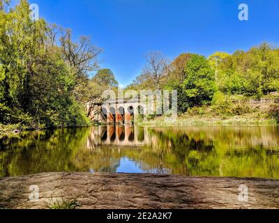 Un beau lac pittoresque avec des reflets des arbres environnants et viaduc lors d'une journée ensoleillée de ciel bleu. Étang 7 sur Hampstead Heath appelé Viaduct Pond. Banque D'Images