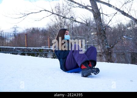 Adolescente dans un masque protecteur glissant sur la luge plaque Banque D'Images