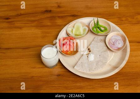 Bhakari, pain indien, déjeuner servi avec du pain, des tranches de tomates et de concombres, des rondelles d'oignon, du beurre et du lait au beurre. Vue en angle supérieur, prise de vue en studio Banque D'Images