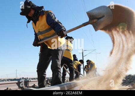 (210113) -- AKSAY, 13 janvier 2021 (Xinhua) -- les cheminots nettoient le sable dans le comté autonome de Kazak, dans la province de Gansu, dans le nord-ouest de la Chine, 12 janvier 2021. Le chemin de fer de Dunhuang, qui a ouvert ses portes en décembre 2019, croise les chemins de fer existants, notamment le chemin de fer de Lanzhou-Qinghai, le chemin de fer de Qinghai-Tibet et le chemin de fer de Lanzhou-Xinjiang, pour former le premier réseau de chemin de fer circulaire dans la région nord-ouest. Parmi eux, la section de Yangguan à Shashangou est située à Shazaoyuan, un lieu connu pour son fort vent de travers dans le comté autonome de Kazak d'Aksay. Le sable enterrait le tr Banque D'Images