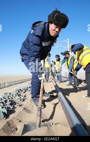 (210113) -- AKSAY, 13 janvier 2021 (Xinhua) -- les cheminots nettoient le sable dans le comté autonome de Kazak, dans la province de Gansu, dans le nord-ouest de la Chine, 12 janvier 2021. Le chemin de fer de Dunhuang, qui a ouvert ses portes en décembre 2019, croise les chemins de fer existants, notamment le chemin de fer de Lanzhou-Qinghai, le chemin de fer de Qinghai-Tibet et le chemin de fer de Lanzhou-Xinjiang, pour former le premier réseau de chemin de fer circulaire dans la région nord-ouest. Parmi eux, la section de Yangguan à Shashangou est située à Shazaoyuan, un lieu connu pour son fort vent de travers dans le comté autonome de Kazak d'Aksay. Le sable enterrait le tr Banque D'Images