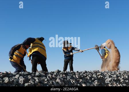 (210113) -- AKSAY, 13 janvier 2021 (Xinhua) -- les cheminots nettoient le sable dans le comté autonome de Kazak, dans la province de Gansu, dans le nord-ouest de la Chine, 12 janvier 2021. Le chemin de fer de Dunhuang, qui a ouvert ses portes en décembre 2019, croise les chemins de fer existants, notamment le chemin de fer de Lanzhou-Qinghai, le chemin de fer de Qinghai-Tibet et le chemin de fer de Lanzhou-Xinjiang, pour former le premier réseau de chemin de fer circulaire dans la région nord-ouest. Parmi eux, la section de Yangguan à Shashangou est située à Shazaoyuan, un lieu connu pour son fort vent de travers dans le comté autonome de Kazak d'Aksay. Le sable enterrait le tr Banque D'Images