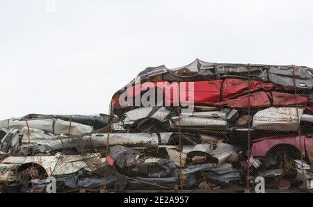 Un tas de voitures écrasées maintenues à l'arrière d'un camion plat par un filet métallique et des chaînes. Le ciel est nuageux. Il y a de la place pour le texte. Banque D'Images