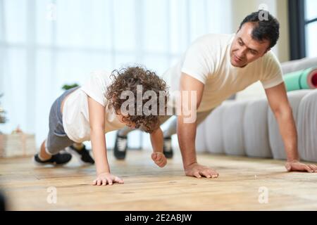 Un père latin sportif d'âge moyen apprend à son fils à faire des retouches tout en passant du temps ensemble à la maison. Mode de vie sain, sport à la maison concept Banque D'Images