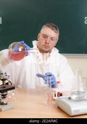 Un professeur de chimie à l'école verse des produits chimiques d'une fiole dans un verre. Banque D'Images