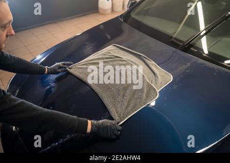 Un agent de lavage de voiture essuie la voiture après le lavage avec une serviette en microfibre. Lavage de voiture professionnel Banque D'Images