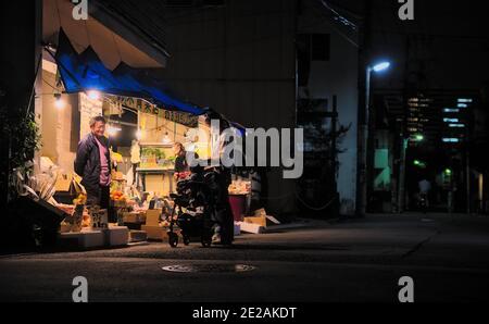 Suginami, Tokyo, Japon - septembre 30 2020 : vue de nuit d'un couple avec un bébé dans une poussette s'arrêtant pour faire du shopping dans un petit magasin de produits sur le côté Banque D'Images