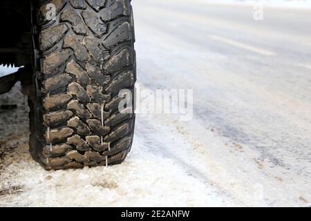 Roue de voiture recouverte de glace et de boue sur une route enneigée. Pneus d'hiver, conduite par temps froid et sur glace Banque D'Images