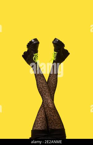 Nouvelles bottes grises avec lacets jaune vif sur les longues jambes croisées de femme en collants gris isolés sur fond jaune. Pop art concept avec H Banque D'Images