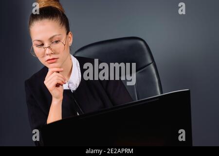 Photo agrandie d'une femme d'affaires avec des lunettes regardant sérieusement l'ordinateur portable. Arrière-plan gris. Banque D'Images