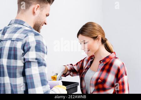 bonne jeune femme mettant rouleau de peinture dans le plateau presque flou homme au premier plan à l'intérieur Banque D'Images