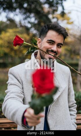 Gros plan vertical d'un mâle tenant et mordant la tige De roses rouges-concept Saint-Valentin Banque D'Images