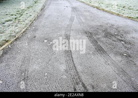 gros plan des traces de pneus du véhicule sur route glacée avec l'herbe s'enfond à l'extérieur en hiver après un gel dur Banque D'Images