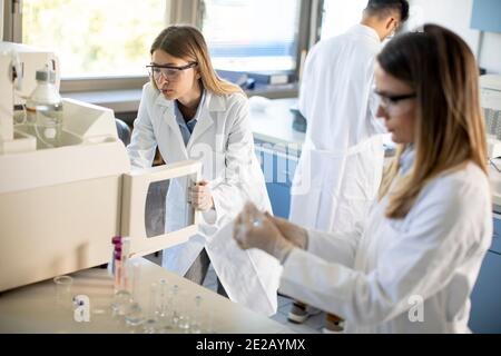 Jeunes femmes scientifiques dans un flacon de mise en blouse de laboratoire blanc avec un échantillon pour une analyse sur un système d'ionchromatographie en laboratoire biomédical Banque D'Images