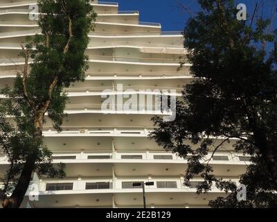 Détail d'un bâtiment blanc moderne avec balcons et arbres verts au premier plan. Photo de bas en haut Banque D'Images