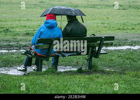 WIMBLEDON LONDRES, ROYAUME-UNI 13 JANVIER 2021. Deux hommes qui se rantent sous un parapluie sur Wimbledon Common lors d'une journée froide et humide à Londres. Les gens se rencontrent encore et s'exercent à l'extérieur pendant le confinement national malgré les avertissements du gouvernement de rester à la maison et à distance sociale. Credit: amer ghazzal / Alamy Live News Banque D'Images